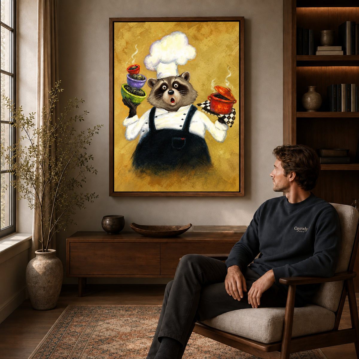 playful raccoon chef canvas art in a walnut frame above a console beside a seated man.