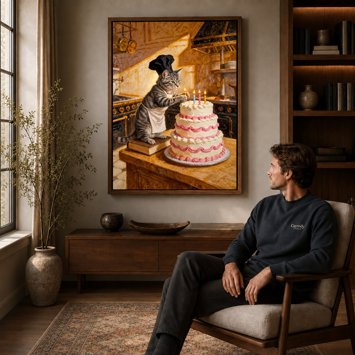 warm birthday baker cat canvas art in a walnut frame above a console beside a seated man.