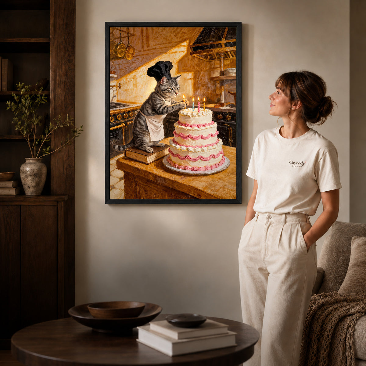 warm birthday baker cat canvas art in a black frame beside a woman and round wooden table.