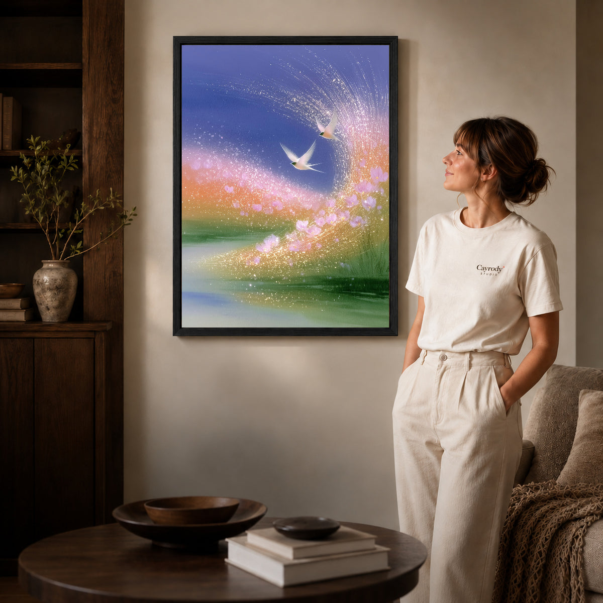 luminous meadow birds canvas art in a black frame beside a woman and round wooden table.