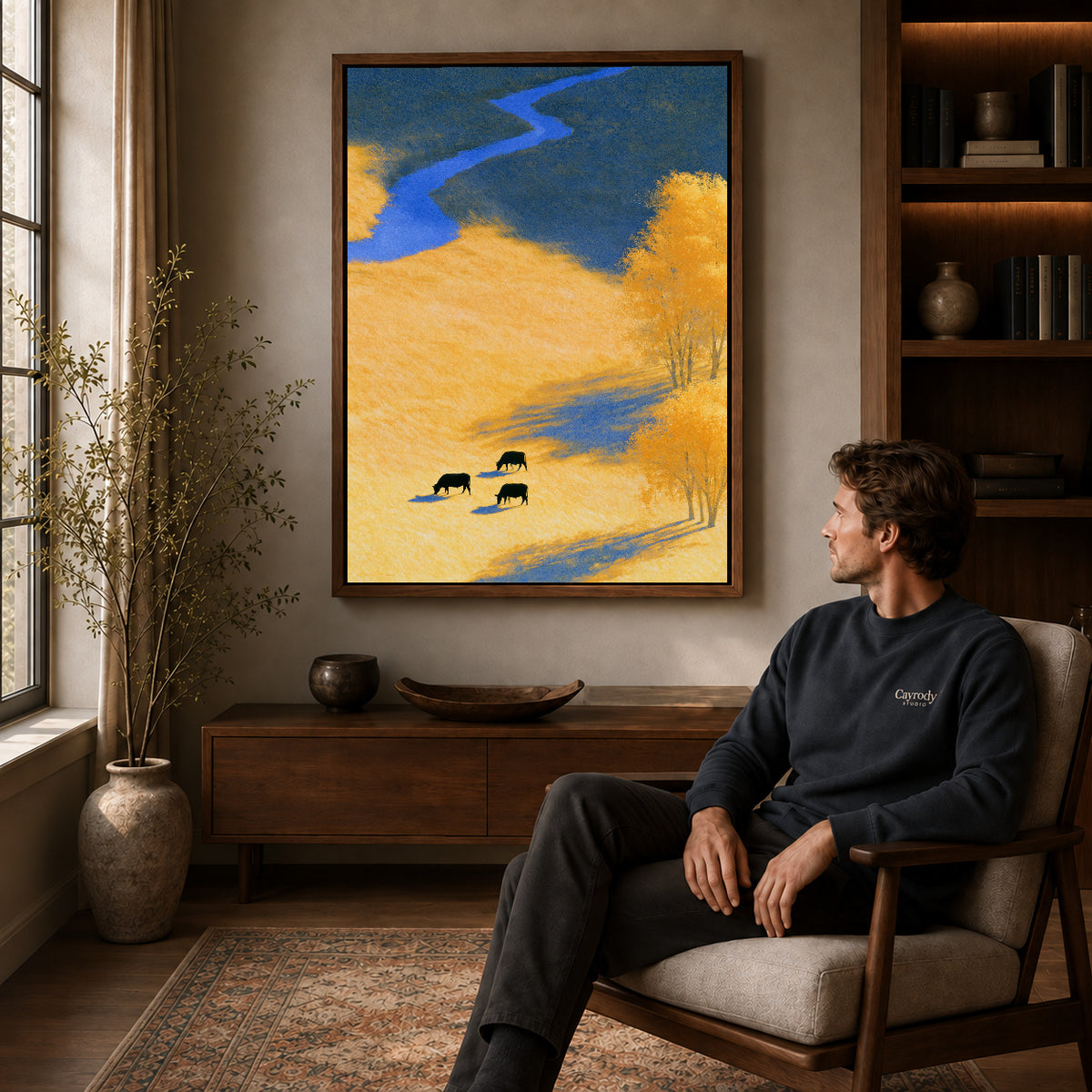 golden meadow cows canvas art in a walnut frame above a console beside a seated man.