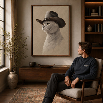 quiet cowboy cat canvas art in a walnut frame above a console beside a seated man.
