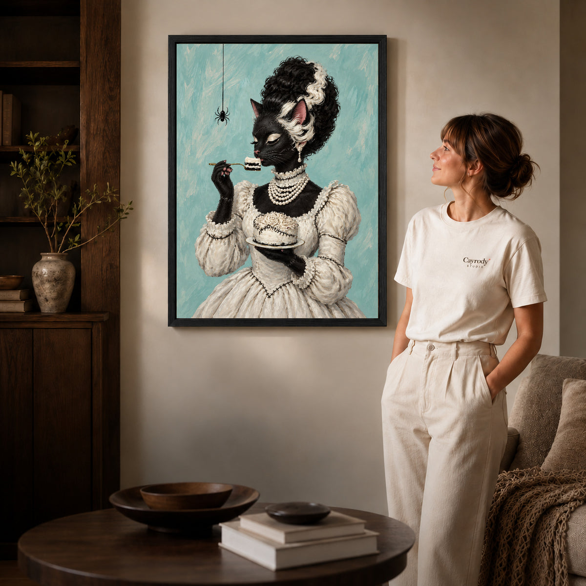 gothic cake cat canvas art in a black frame beside a woman and round wooden table.