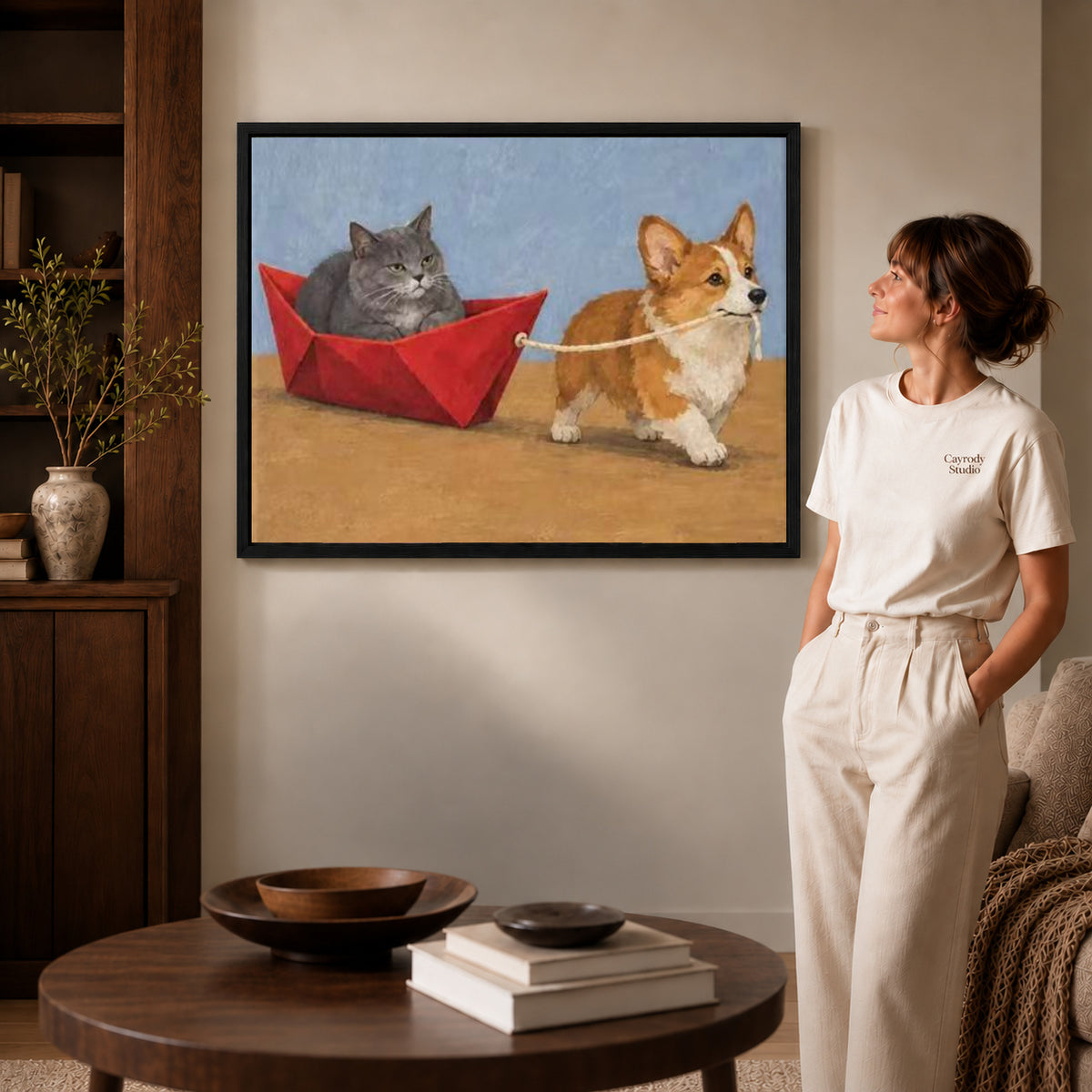 corgi cat boat adventure canvas art in a black frame beside a woman and round wooden table.