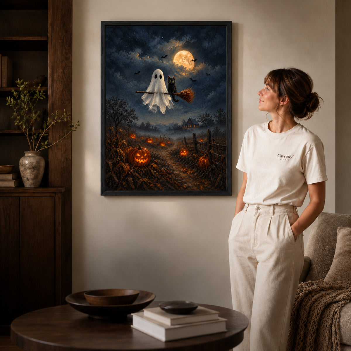 moonlit ghost cat ride canvas art in a black frame beside a woman and round wooden table.