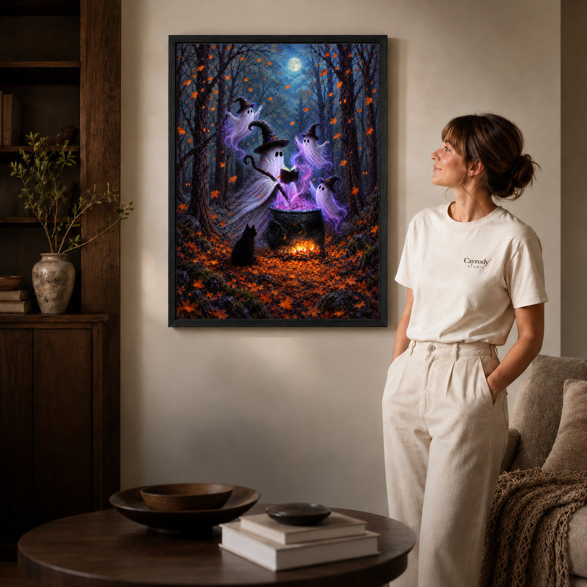 woodland ghost gathering canvas art in a black frame beside a woman and round wooden table.