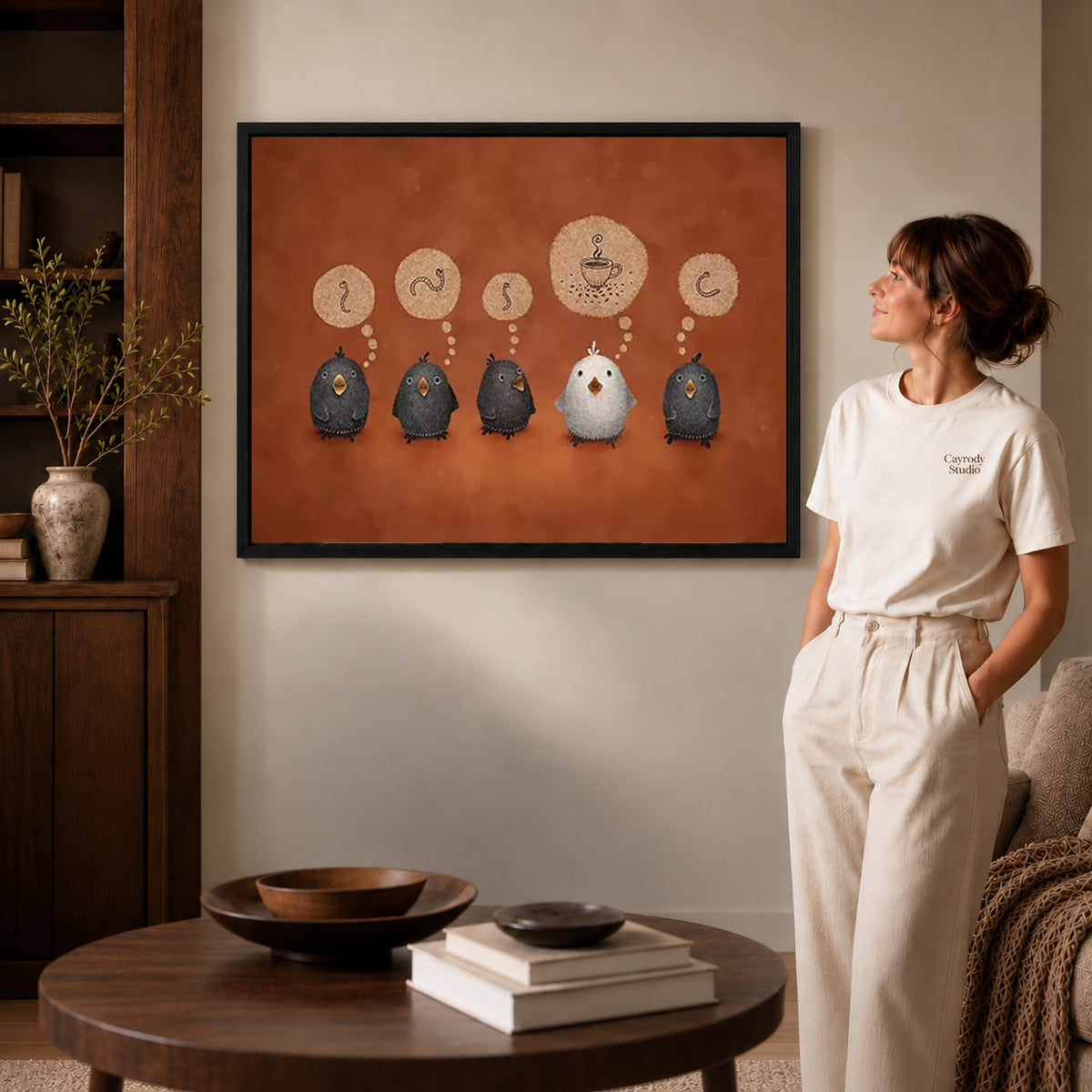 coffee dreaming birds canvas art in a black frame beside a woman and round wooden table.