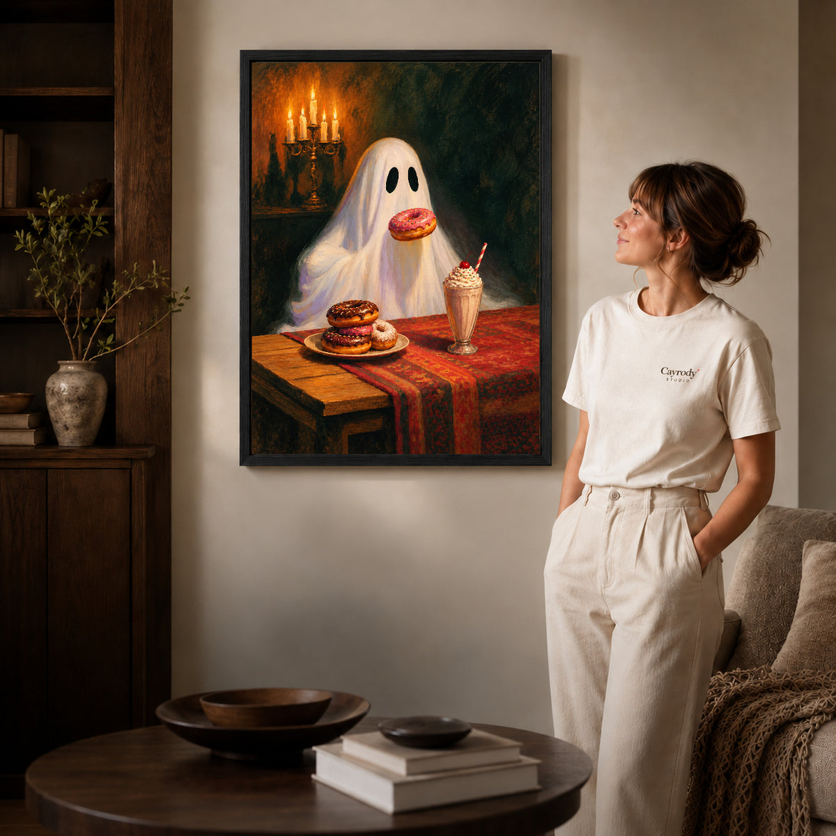 sweet treat ghost canvas art in a black frame beside a woman and round wooden table.