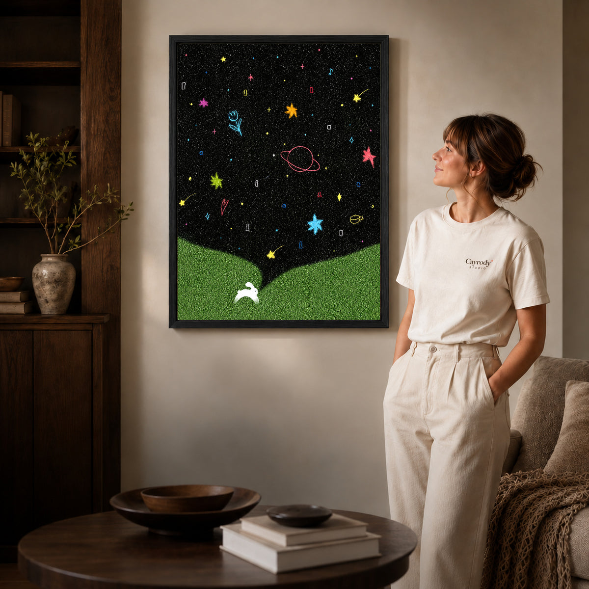 starry rabbit wonderland canvas art in a black frame beside a woman and round wooden table.