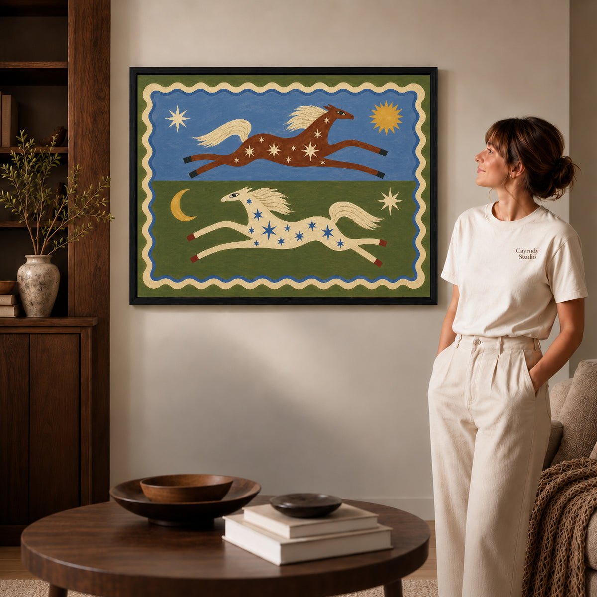 celestial folk horses canvas art in a black frame beside a woman and round wooden table.