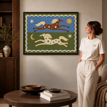 celestial folk horses canvas art in a black frame beside a woman and round wooden table.