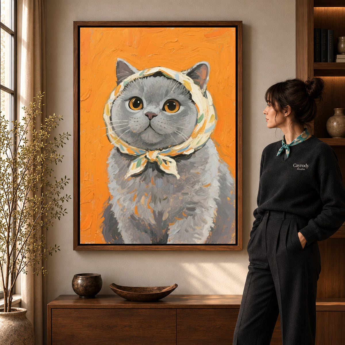 scarf wearing kitten canvas art in a walnut frame beside a standing woman and wooden console.