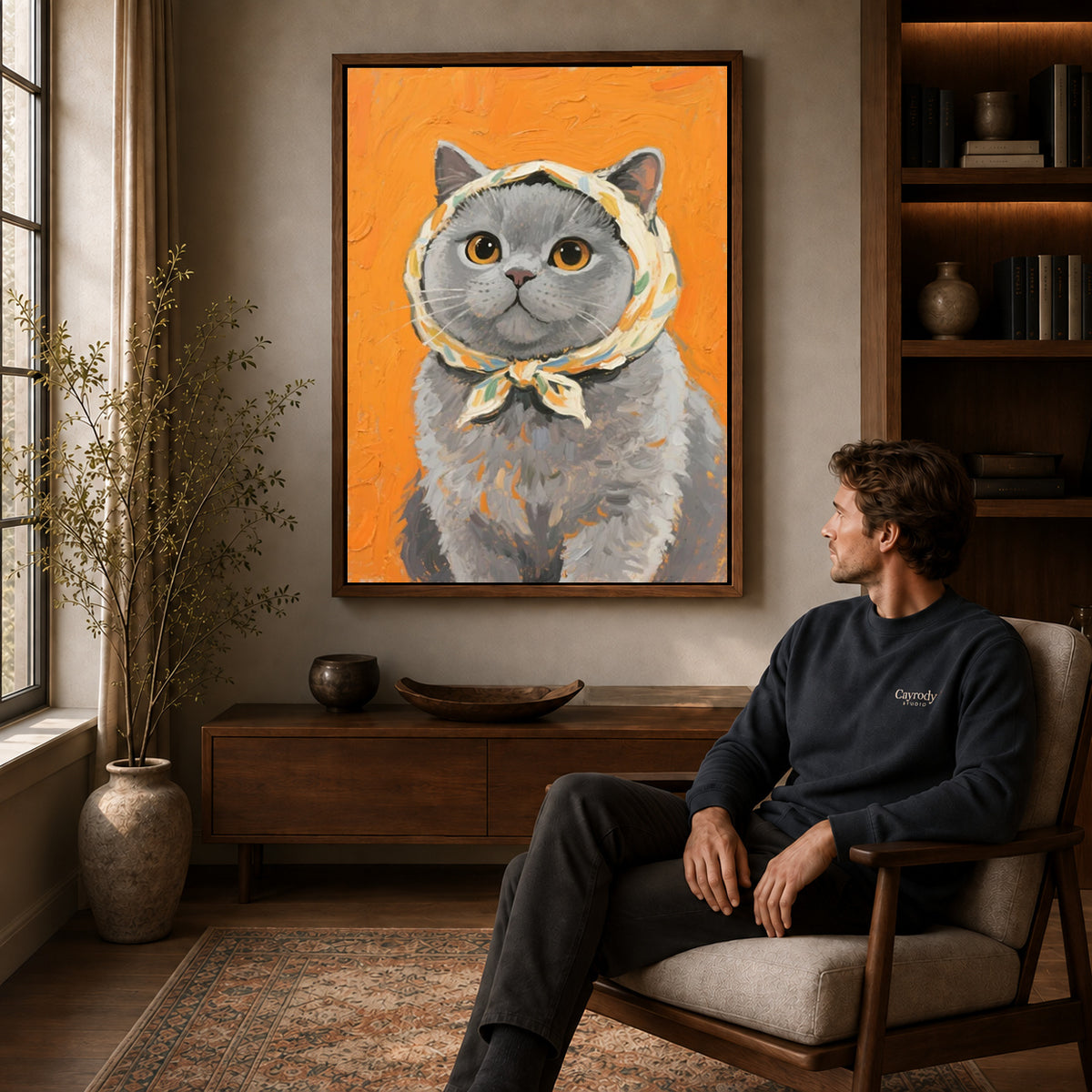 scarf wearing kitten canvas art in a walnut frame above a console beside a seated man.