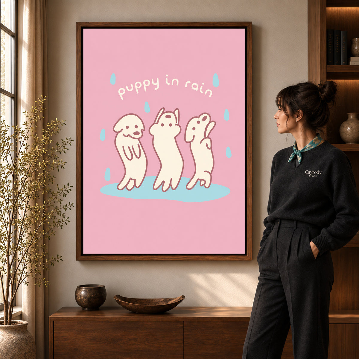 rain dancing puppies canvas art in a walnut frame beside a standing woman and wooden console.