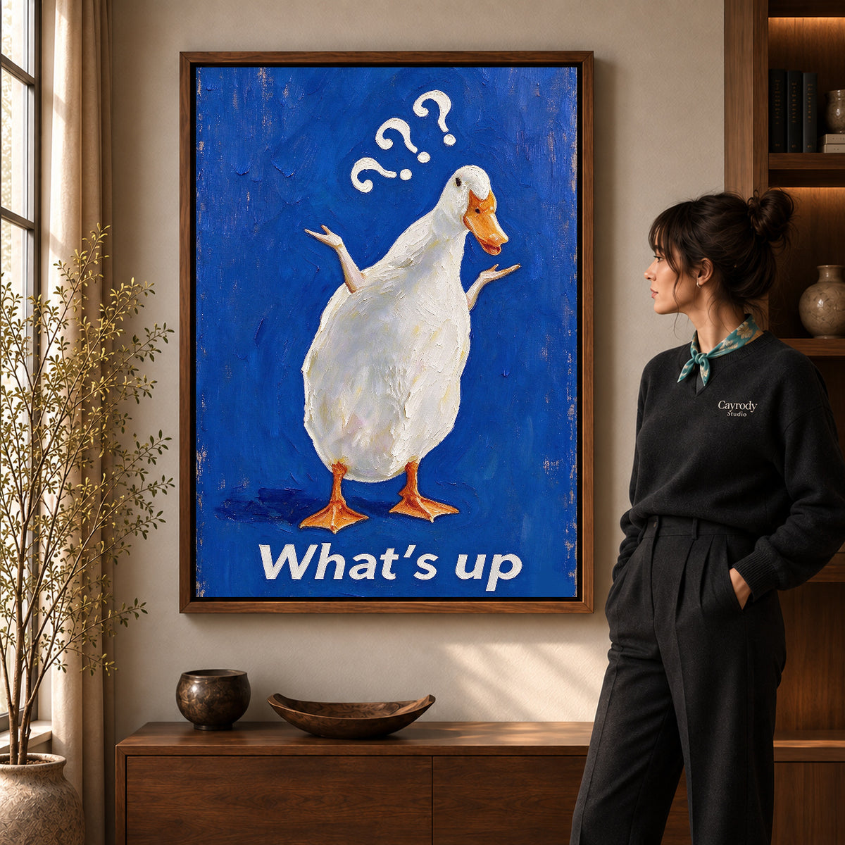 curious shrugging duck canvas art in a walnut frame beside a standing woman and wooden console.