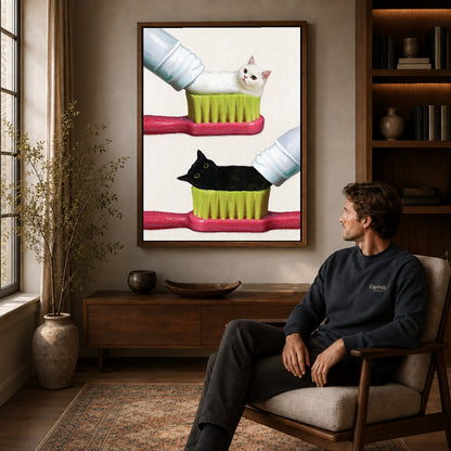 toothpaste kitten duo canvas art in a walnut frame above a console beside a seated man.