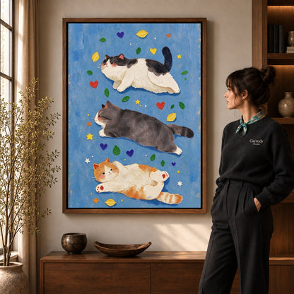 three resting cats canvas art in a walnut frame beside a standing woman and wooden console.
