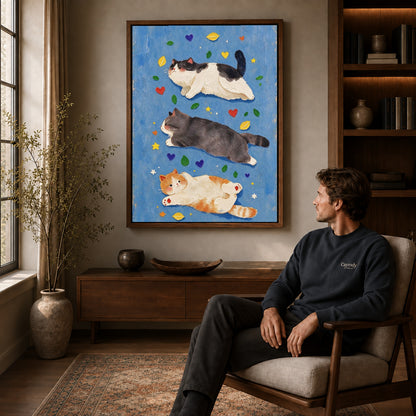 three resting cats canvas art in a walnut frame above a console beside a seated man.