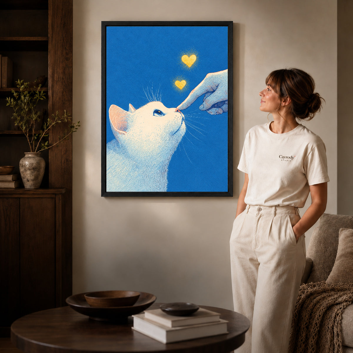 gentle cat greeting canvas art in a black frame beside a woman and round wooden table.