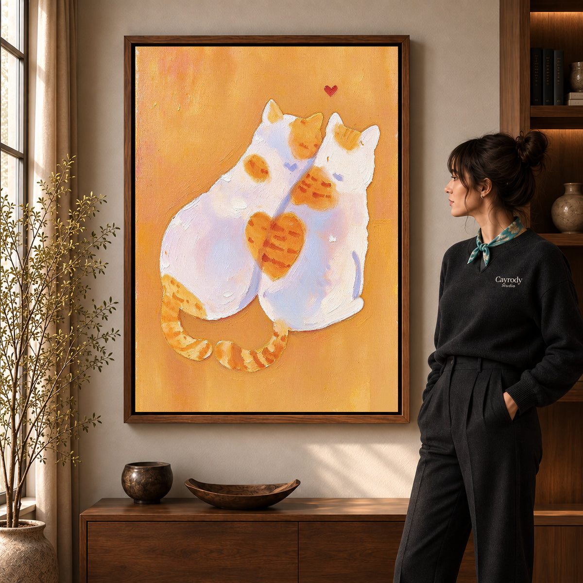 two tender cats canvas art in a walnut frame beside a standing woman and wooden console.