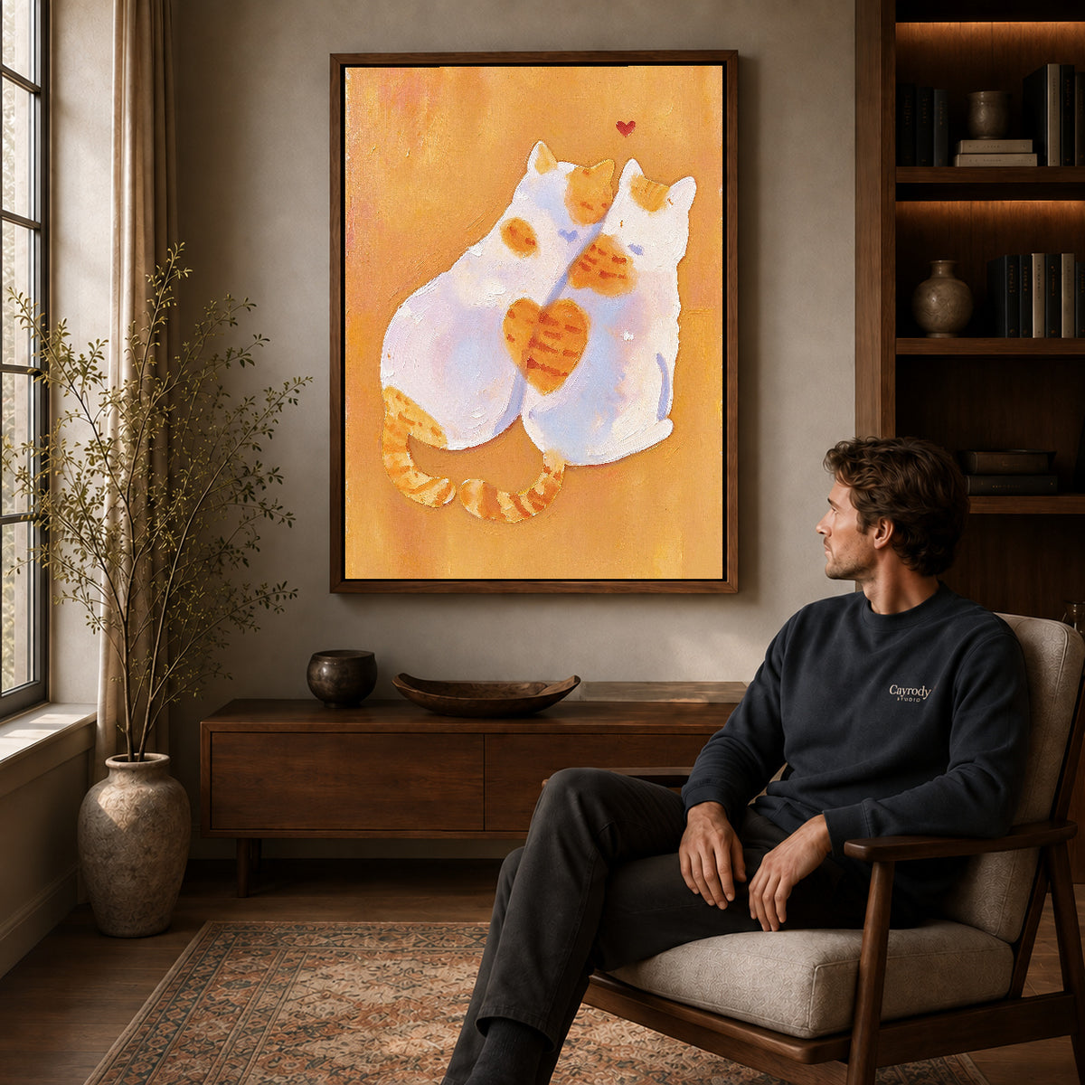 two tender cats canvas art in a walnut frame above a console beside a seated man.