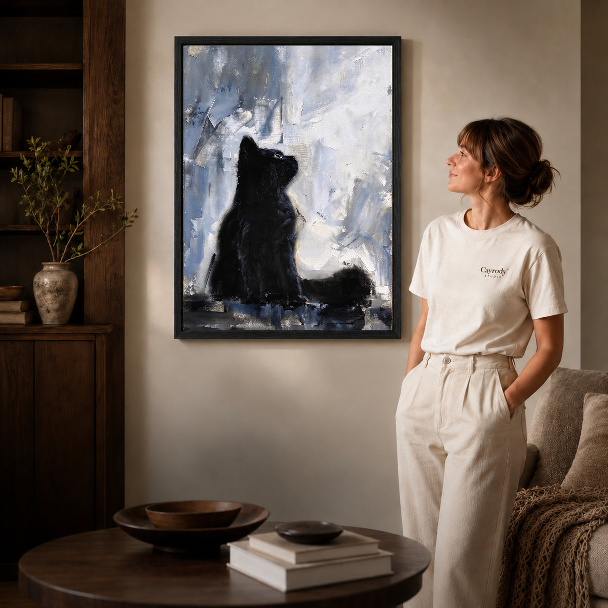 quiet black kitten canvas art in a black frame beside a woman and round wooden table.