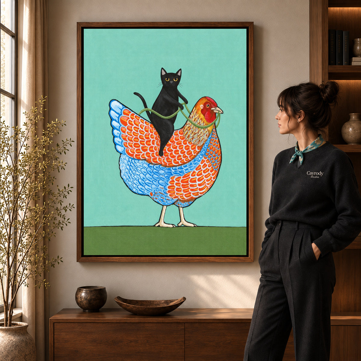 cat riding hen canvas art in a walnut frame beside a standing woman and wooden console.