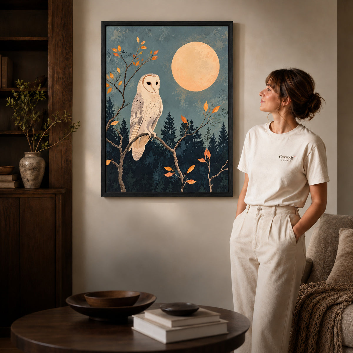moonlit barn owl canvas art in a black frame beside a woman and round wooden table.