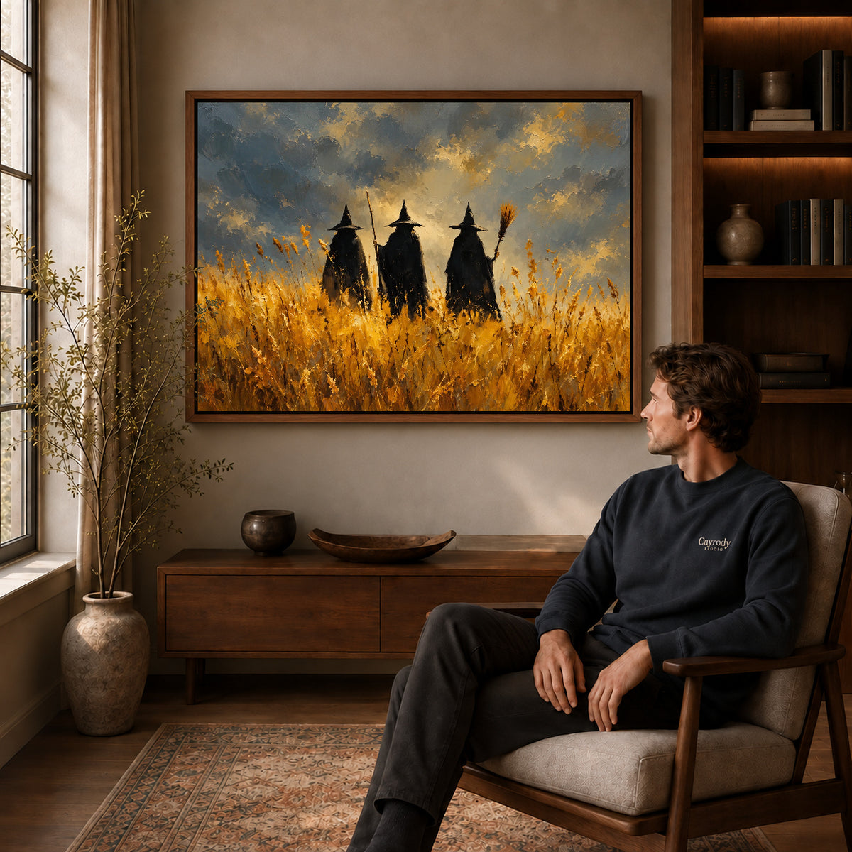 golden meadow witches canvas art in a walnut frame above a console beside a seated man.