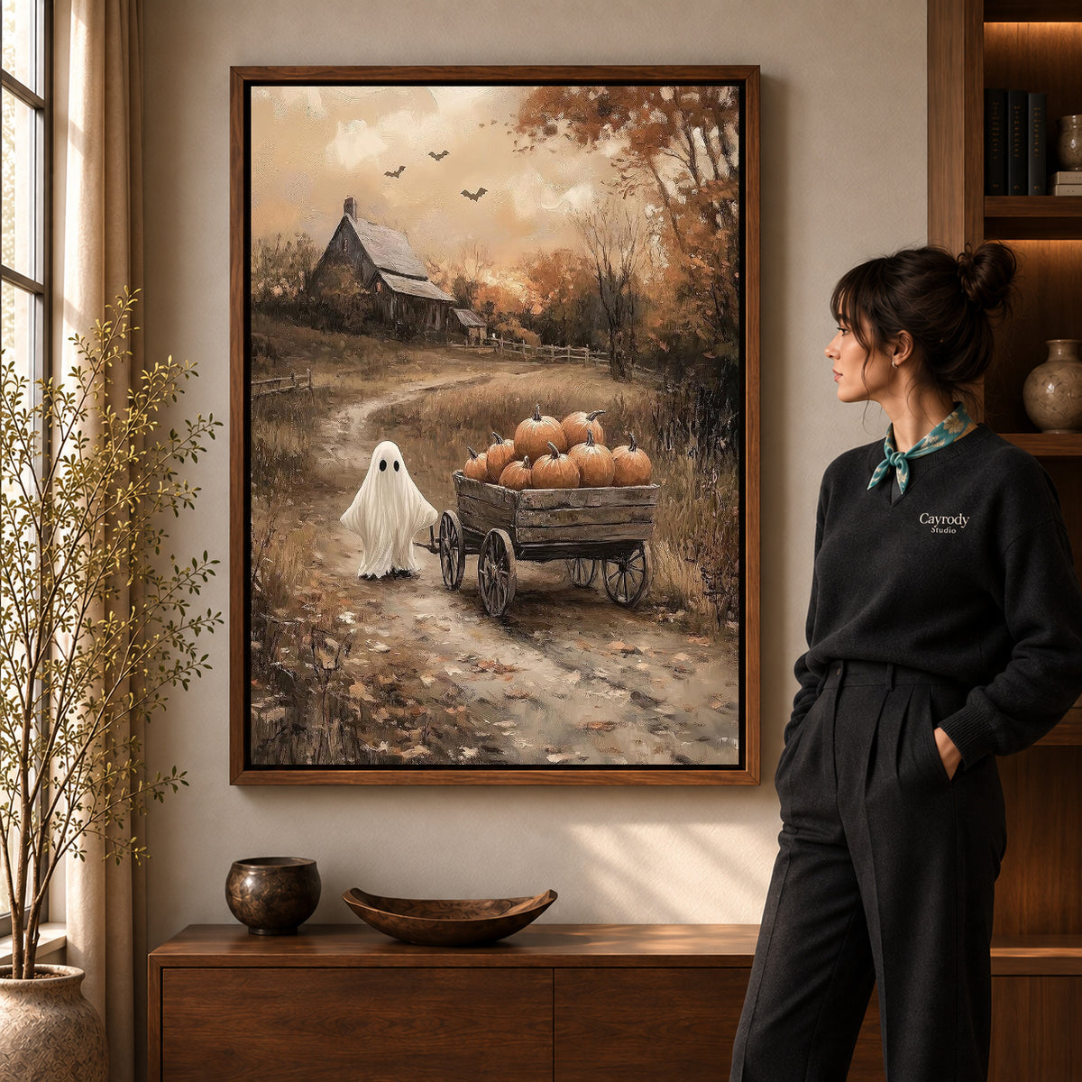 harvest wagon ghost canvas art in a walnut frame beside a standing woman and wooden console.
