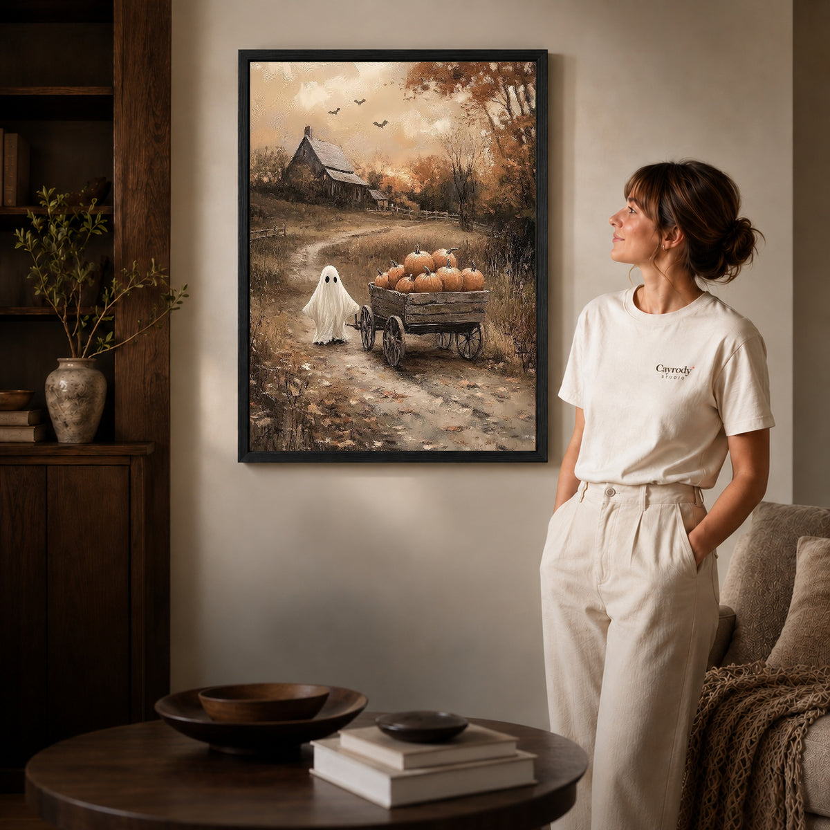 harvest wagon ghost canvas art in a black frame beside a woman and round wooden table.