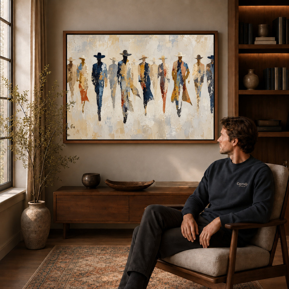 abstract cowboy gathering canvas art in a walnut frame above a console beside a seated man.