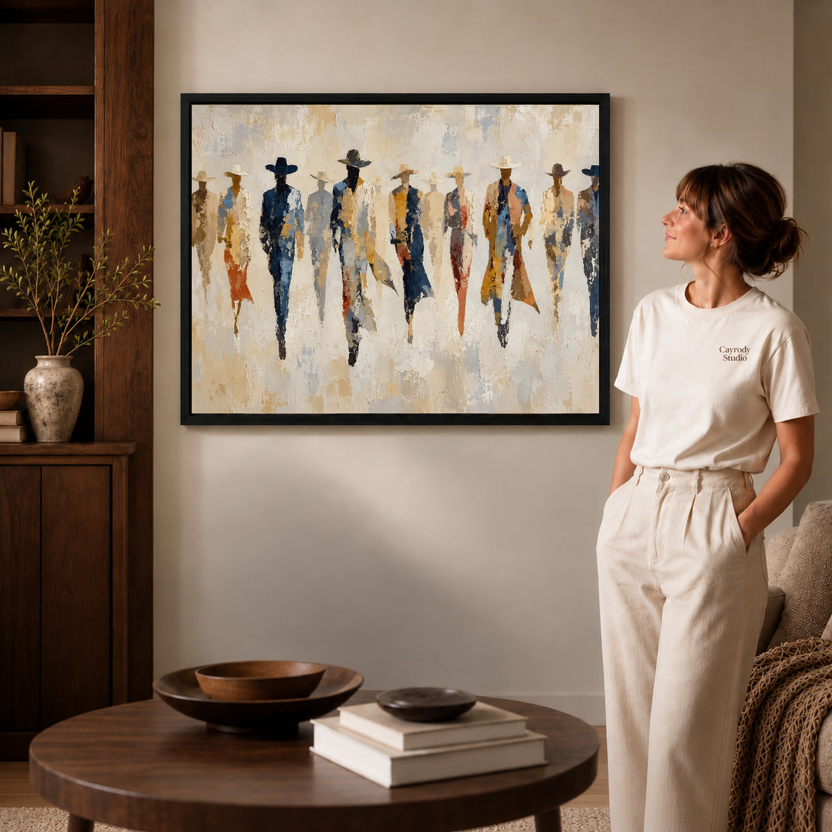 abstract cowboy gathering canvas art in a black frame beside a woman and round wooden table.