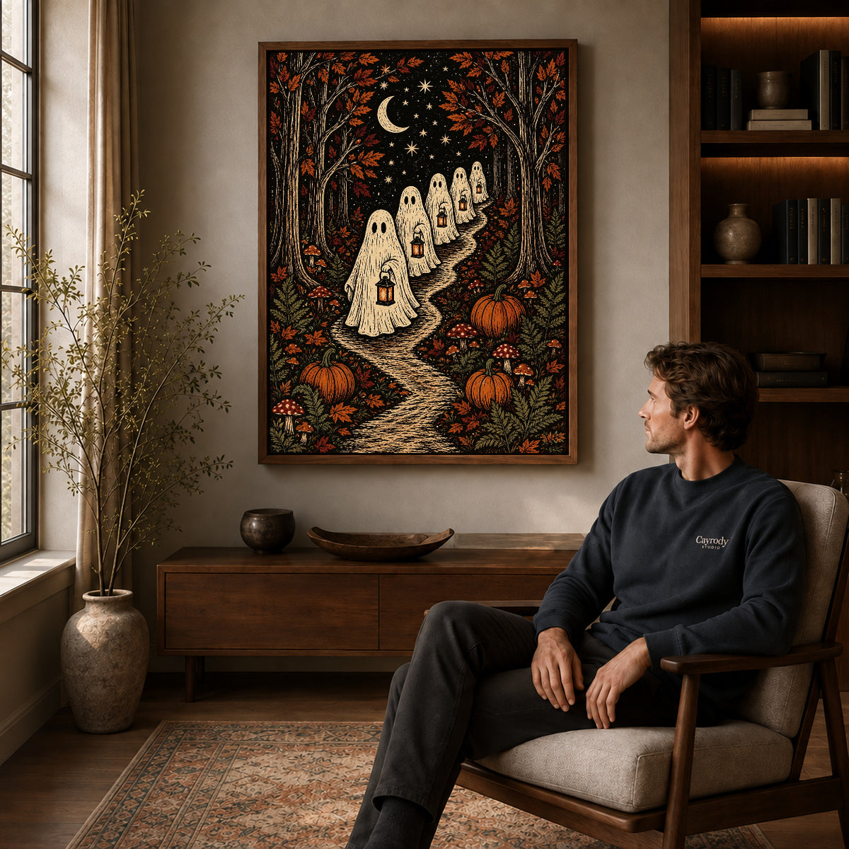 moonlit ghost lanterns canvas art in a walnut frame above a console beside a seated man.