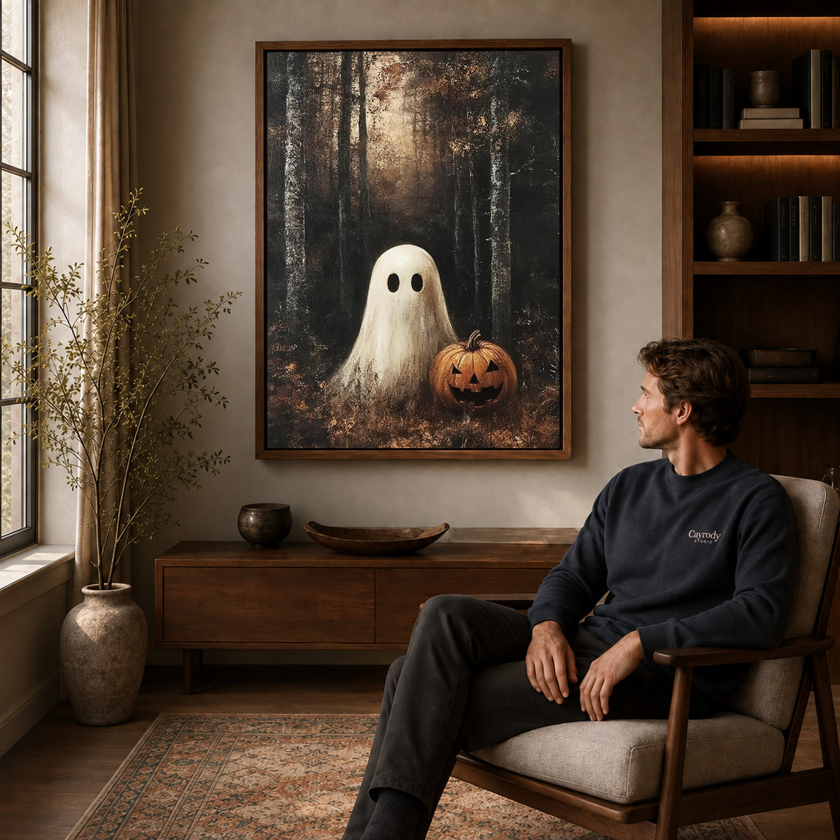 woodland pumpkin ghost canvas art in a walnut frame above a console beside a seated man.