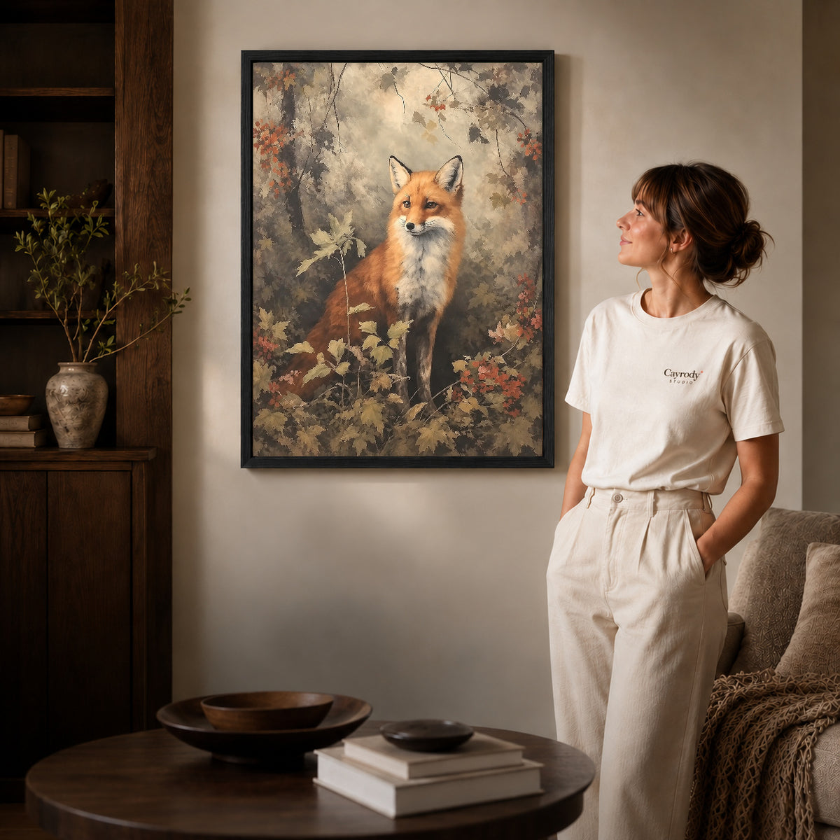 autumn woodland fox canvas art in a black frame beside a woman and round wooden table.