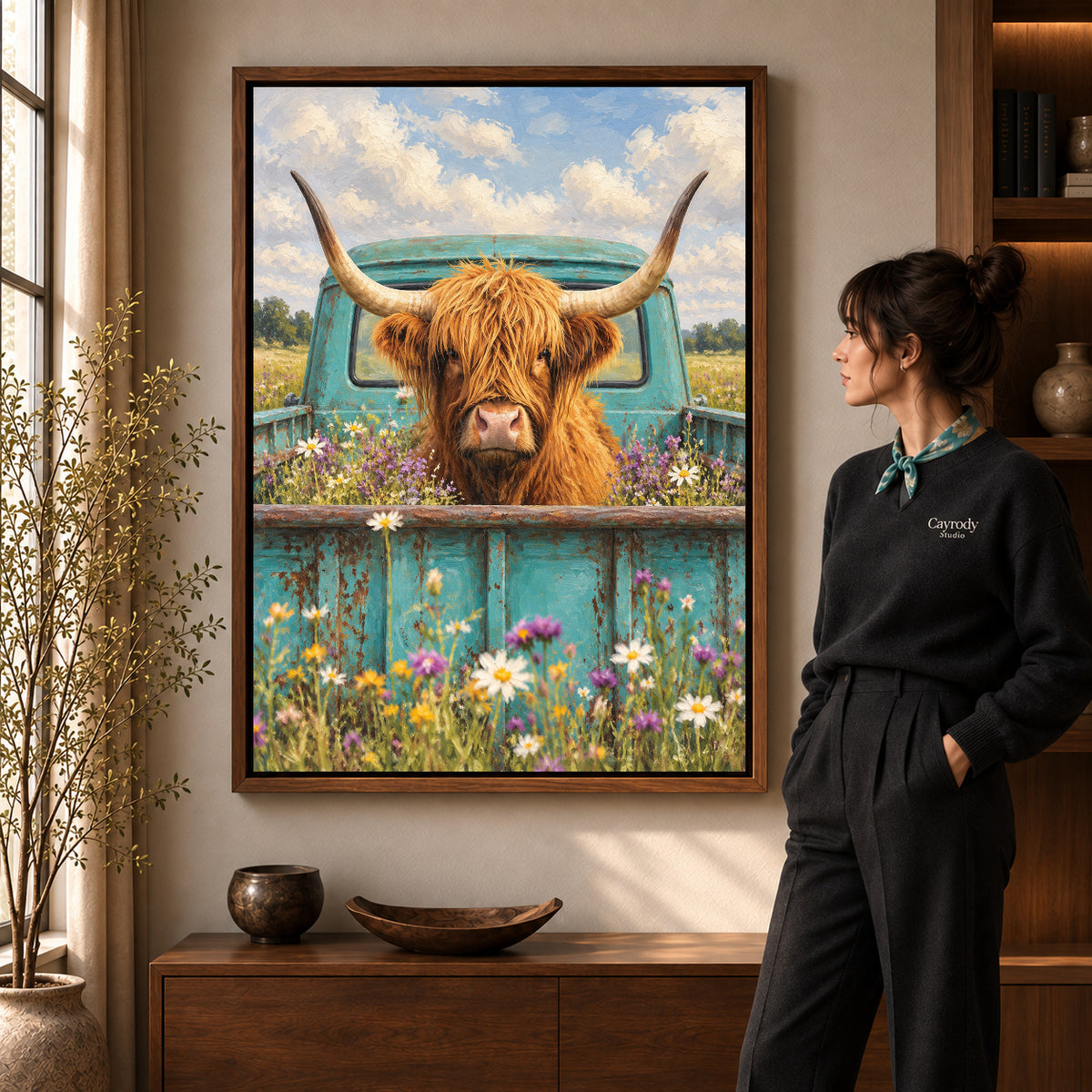 highland cow pickup canvas art in a walnut frame beside a standing woman and wooden console.