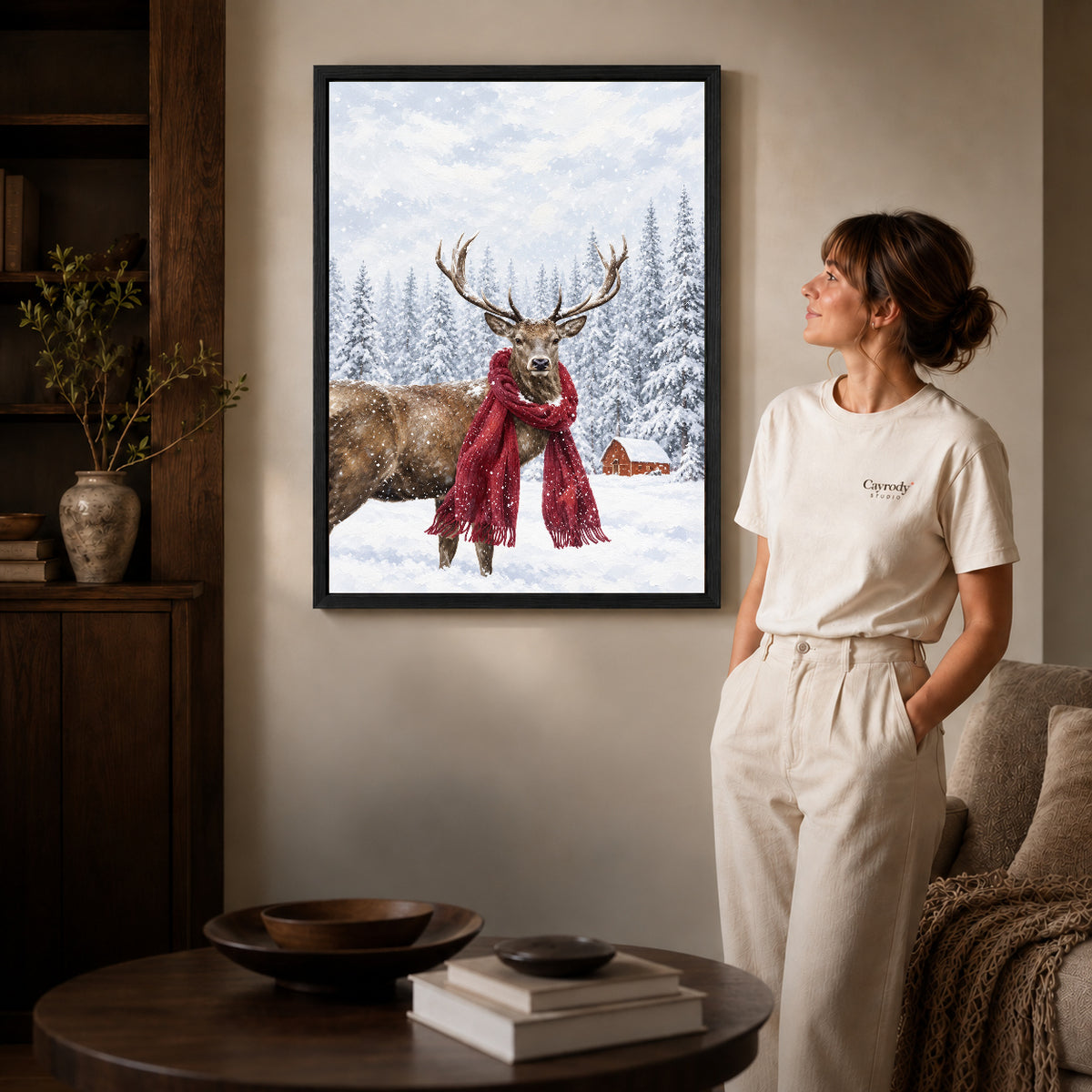 snowy scarf deer canvas art in a black frame beside a woman and round wooden table.