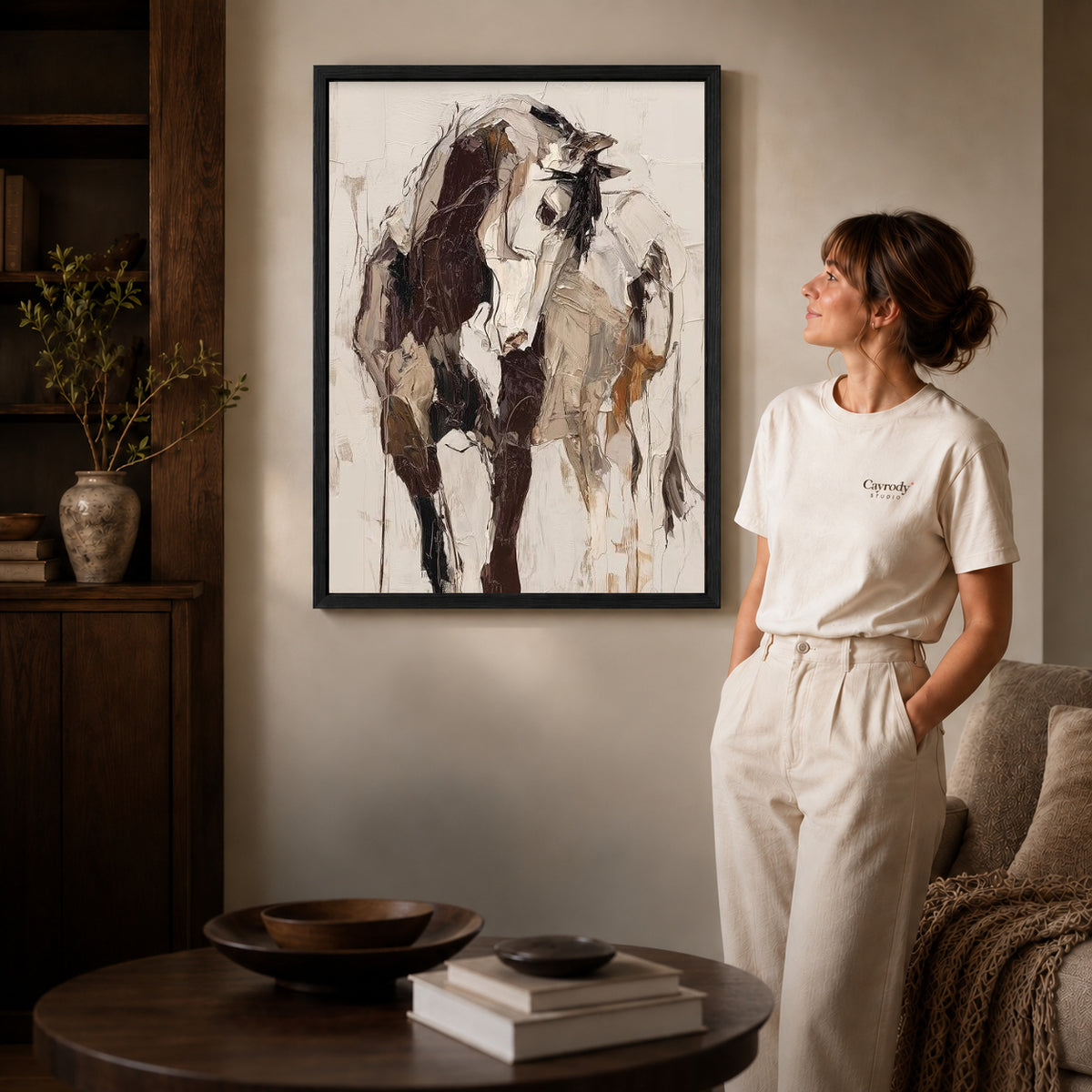 expressive abstract cow canvas art in a black frame beside a woman and round wooden table.