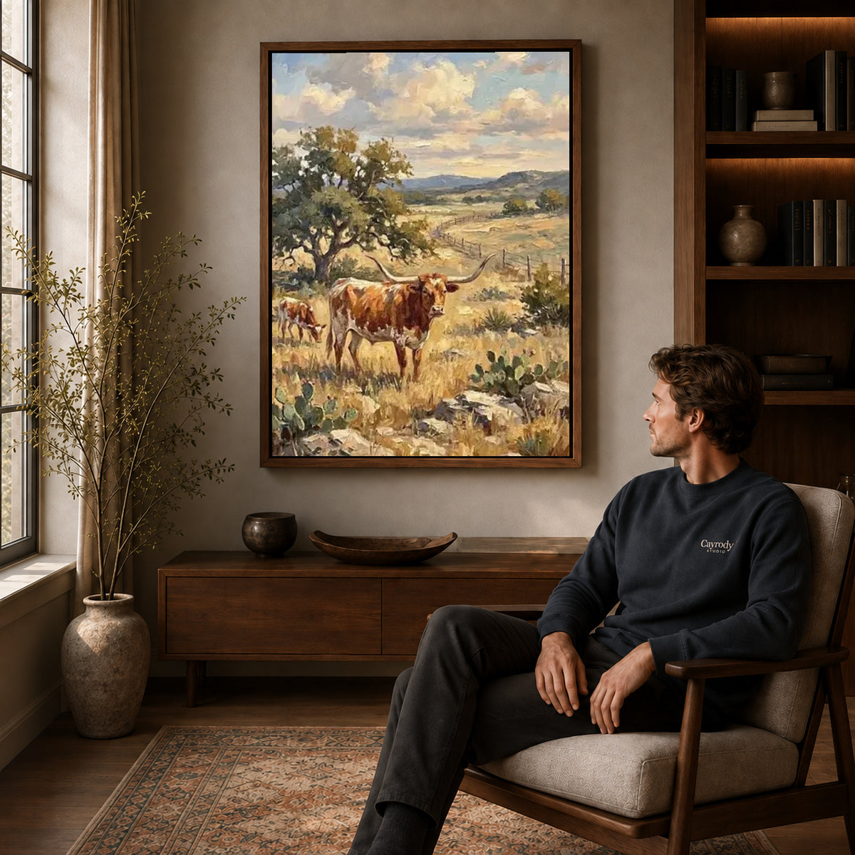 golden longhorn pasture canvas art in a walnut frame above a console beside a seated man.