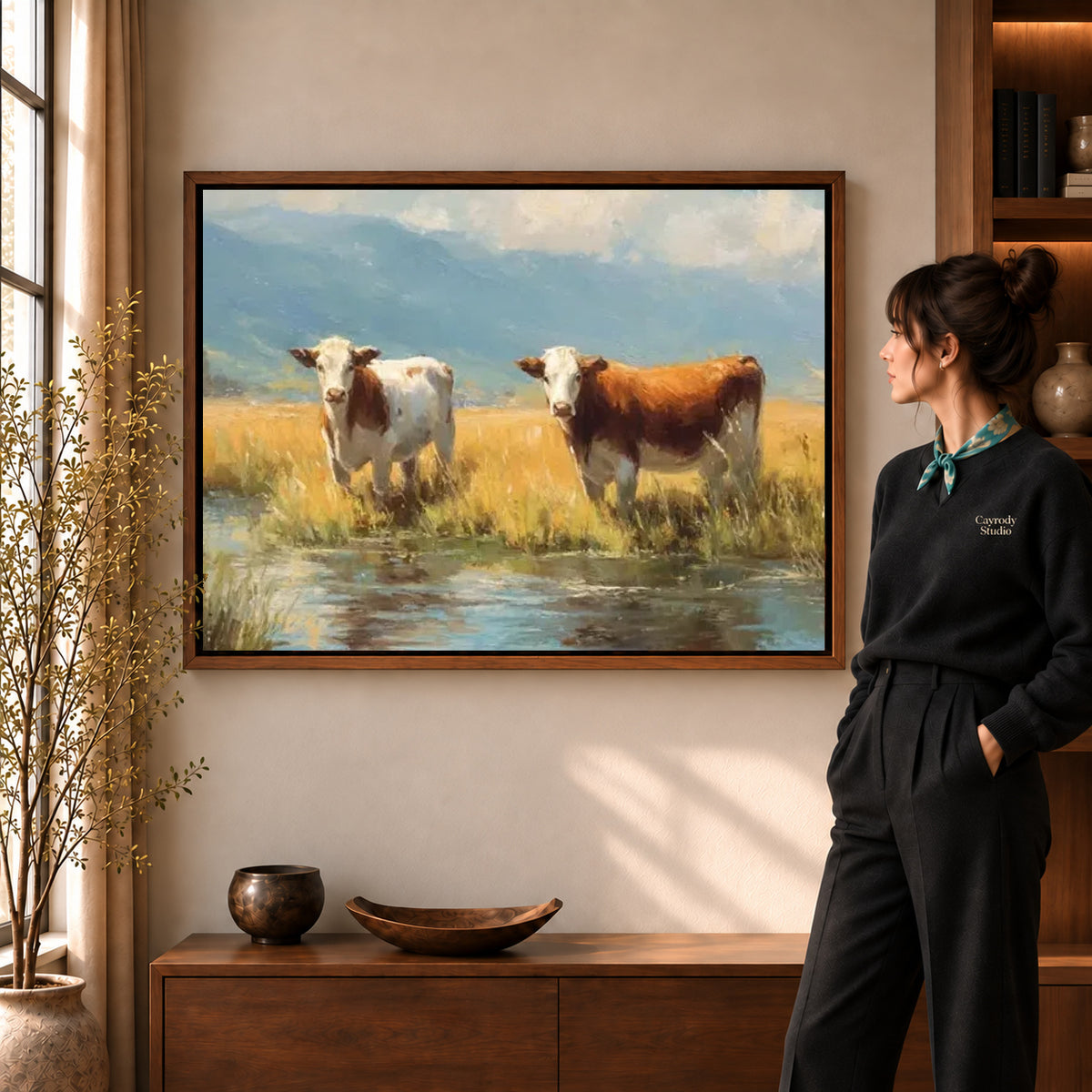 quiet meadow cows canvas art in a walnut frame beside a standing woman and wooden console.