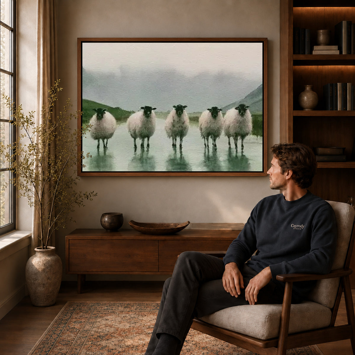rainy valley sheep canvas art in a walnut frame above a console beside a seated man.