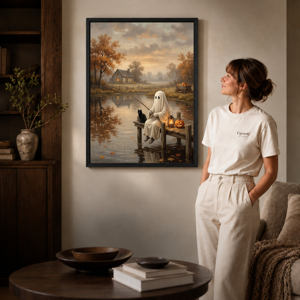 autumn fishing ghost canvas art in a black frame beside a woman and round wooden table.