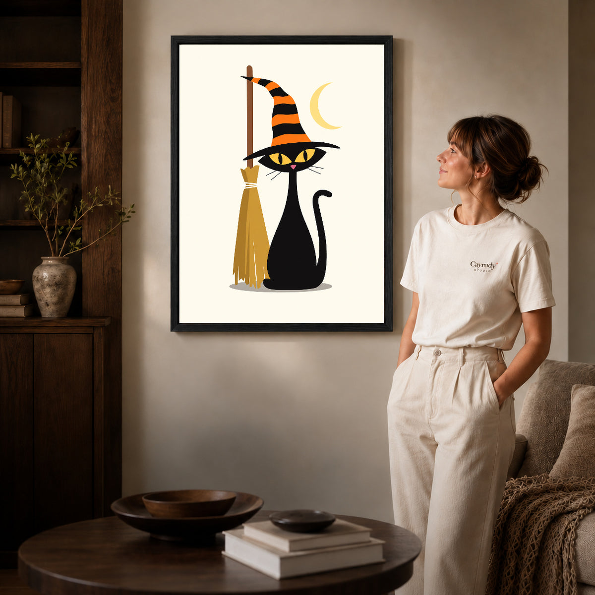 striped hat cat canvas art in a black frame beside a woman and round wooden table.