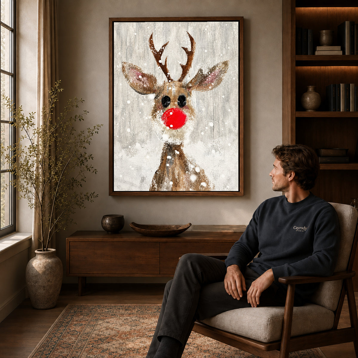 snowy red nose deer canvas art in a walnut frame above a console beside a seated man.