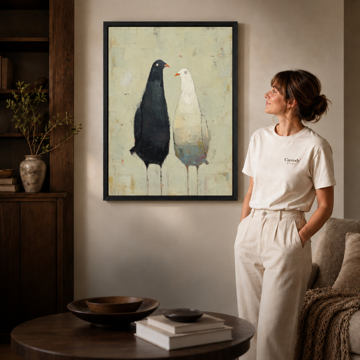 quiet bird companions canvas art in a black frame beside a woman and round wooden table.
