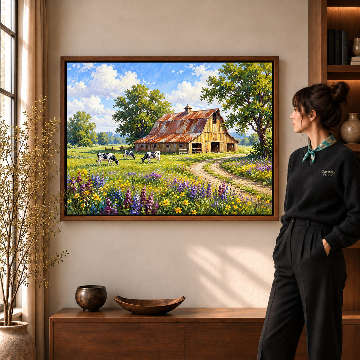 sunlit country barn canvas art in a walnut frame beside a standing woman and wooden console.