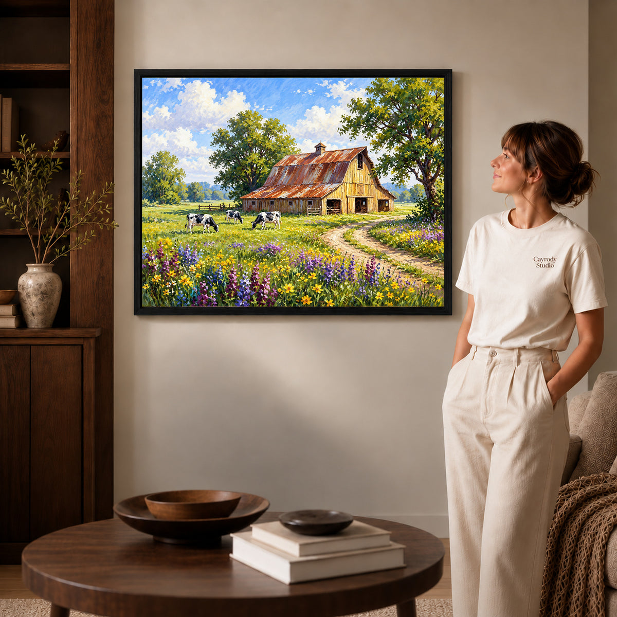 sunlit country barn canvas art in a black frame beside a woman and round wooden table.