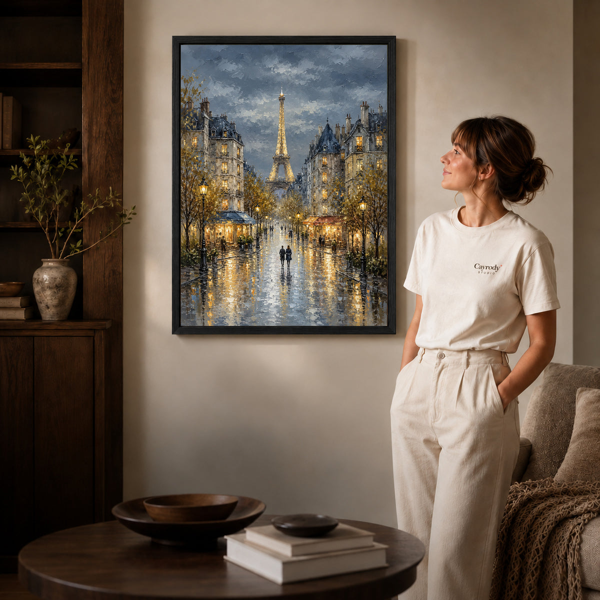 rainy paris evening canvas art in a black frame beside a woman and round wooden table.
