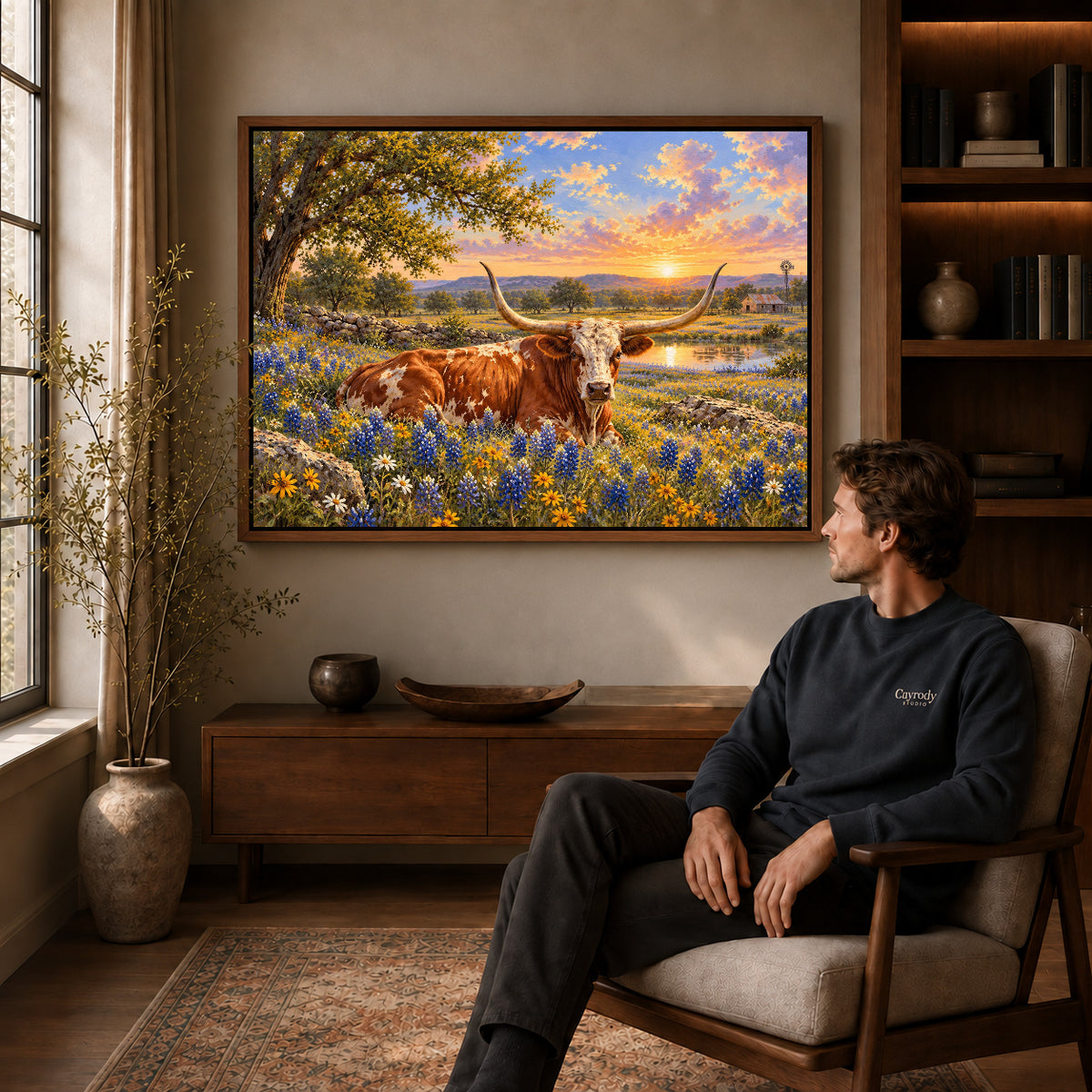 sunset longhorn meadow canvas art in a walnut frame above a console beside a seated man.